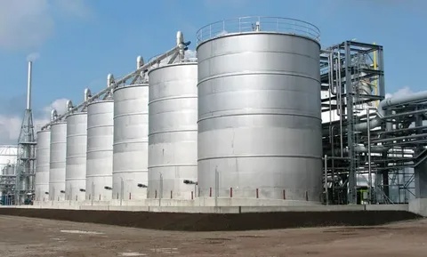 Rail tank cars beside white and blue bulk storage tanks at a terminal